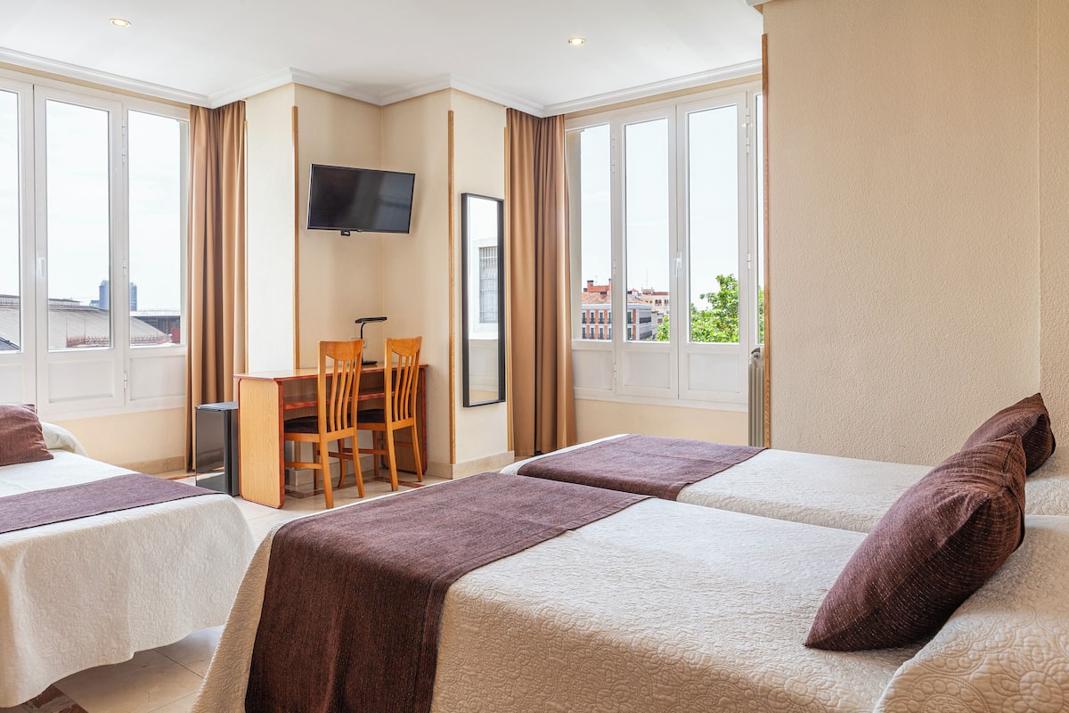 A hotel room with two beds, a desk, a chair, and a TV on the wall.