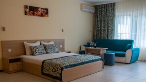 A hotel room with a bed, a small table with two glasses and a bottle, a blue sofa, and a patterned curtain. - Villa Bellevue -Golden Sands Nature Park (Golden Sands)