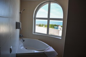 Ein Badezimmer mit einer Badewanne, einem Fenster mit Meerblick und einem Handtuch an der Wand.