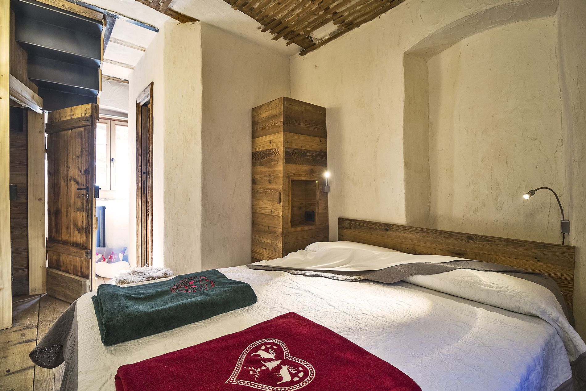 Ein Schlafzimmer mit einem Holzkopfende, einem Bett mit weißer Bettwäsche, einer roten Tagesdecke und einem Nachttisch mit einer Lampe.