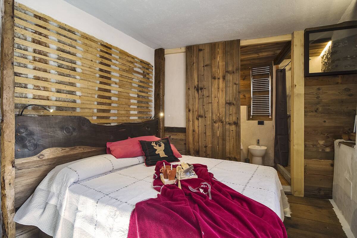 A bedroom with a wooden headboard, a bed with a white quilt, a red blanket, and a pillow with a deer design.