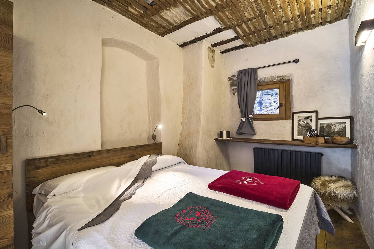 A bedroom with a wooden headboard, a bed with white bedding, a red towel, a green towel with a dragon design, a wooden shelf with pictures, and a window with a curtain.