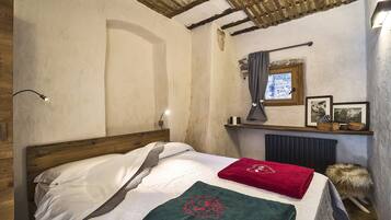 A bedroom with a wooden headboard, a bed with white bedding, a red towel, a green towel with a dragon design, a wooden shelf with pictures, and a window with a curtain.