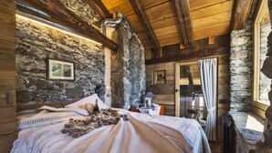 A cozy room with a stone wall, wooden beams, a bed with a blanket, a bottle, and a book. - Maison La Saxe (Courmayeur)