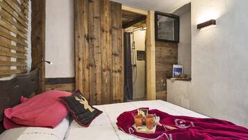 Une chambre avec une porte en bois, un lit recouvert d’une couverture rouge et une petite étagère sur laquelle se trouve une bouteille.