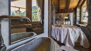 A rustic wooden cabin with a stone sink, a bed with a white blanket, and a view of a mountain landscape through a window. - Maison La Saxe (Courmayeur)