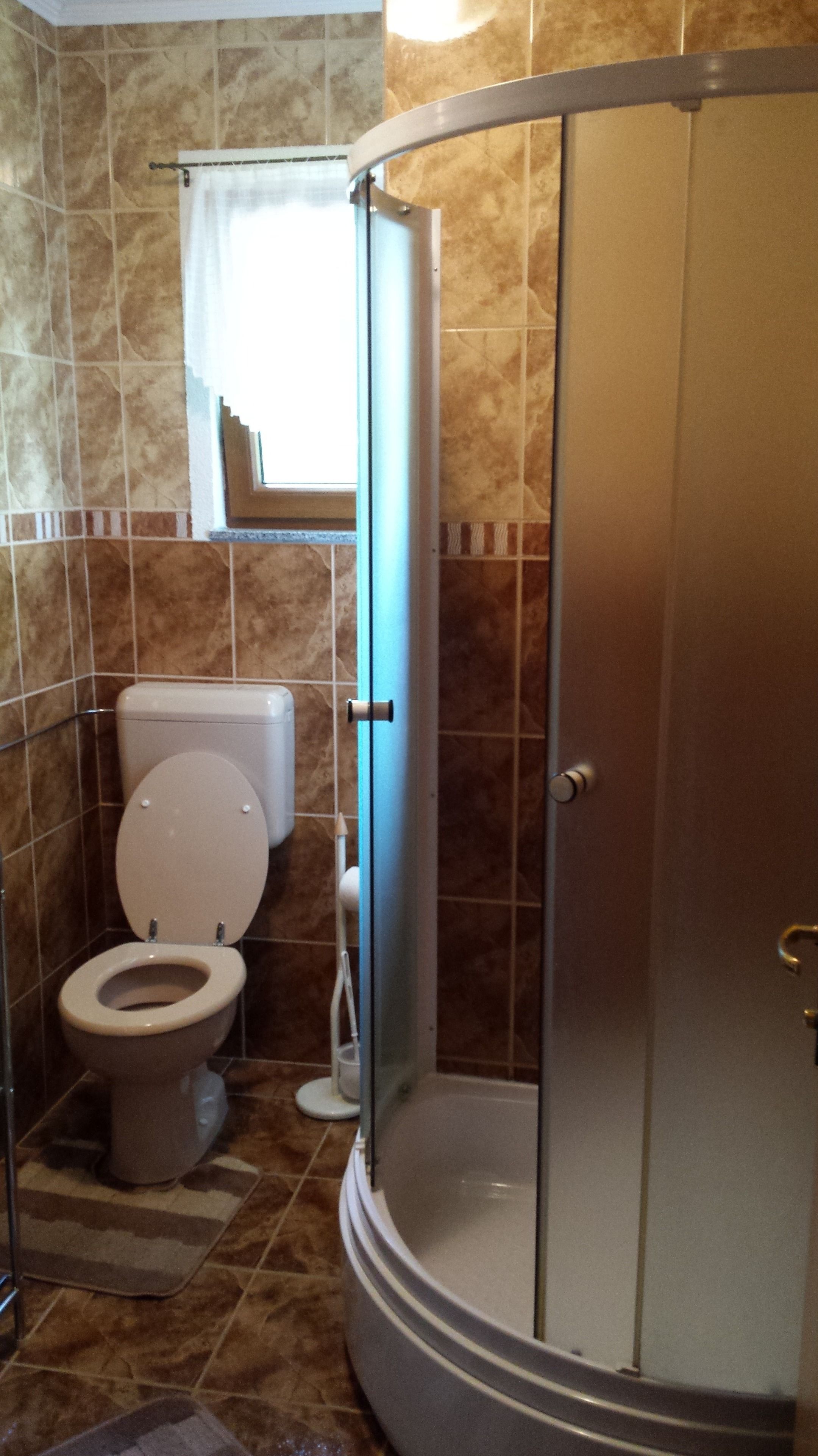 Ein Badezimmer mit Toilette, Dusche und einem Fenster mit Vorhang.