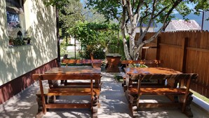 An outdoor patio with wooden tables and benches, surrounded by a wooden fence and trees. - St. George B&B (Plitvicka Jezera)