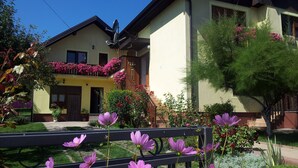 A two-story house with a balcony adorned with pink flowers, a garden with purple flowers, and a wooden fence. - St. George B&B (Plitvicka Jezera)