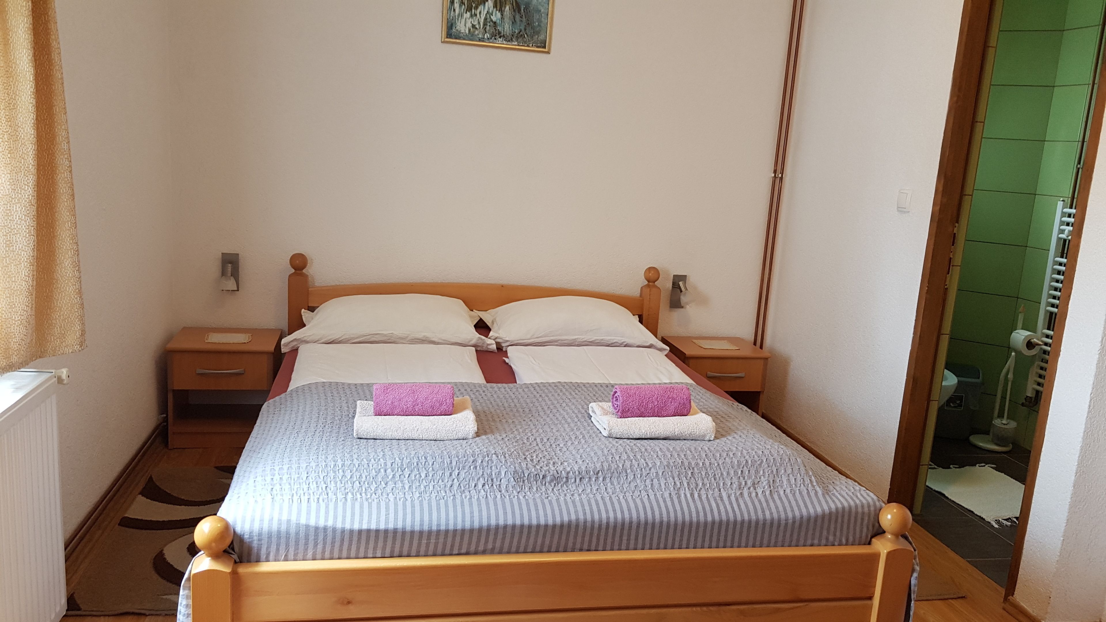Una cama individual con estructura de madera, dos almohadas blancas y dos toallas enrolladas.