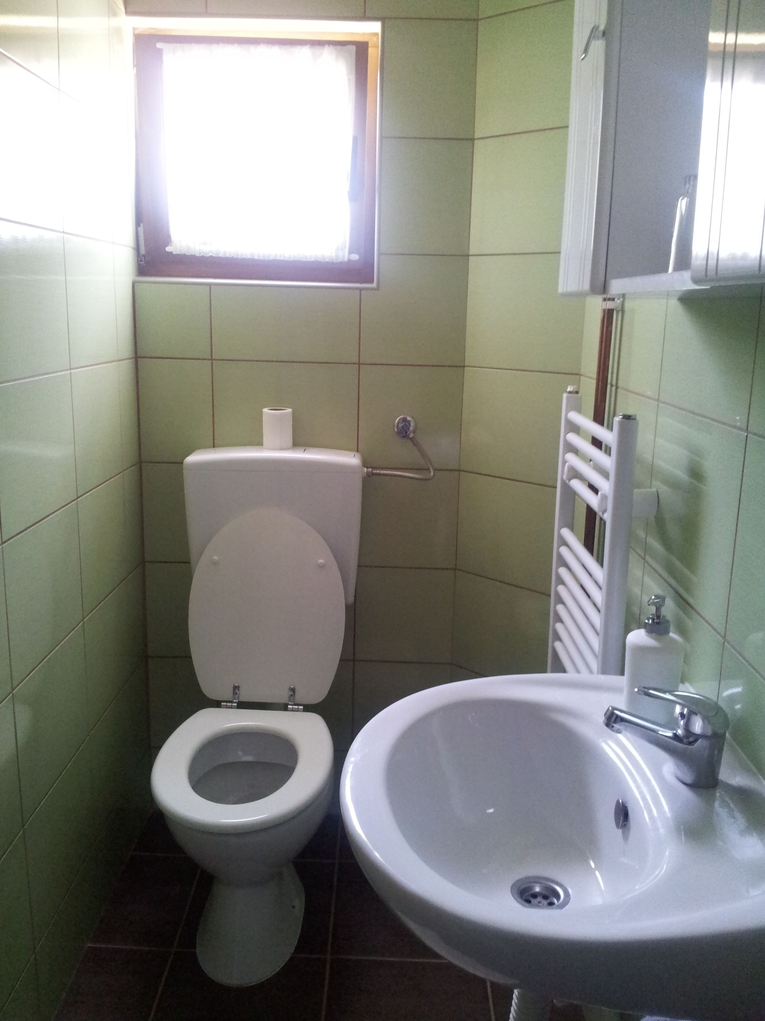 A small bathroom with a toilet, sink, and a window above the toilet.