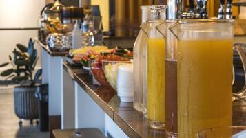 A bar area with a variety of beverages, including a large pitcher of orange juice, a tall glass of iced tea, and a glass of water. There are stools and a counter with a barista behind it.