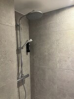 A shower with a handheld showerhead and a wall-mounted control panel.