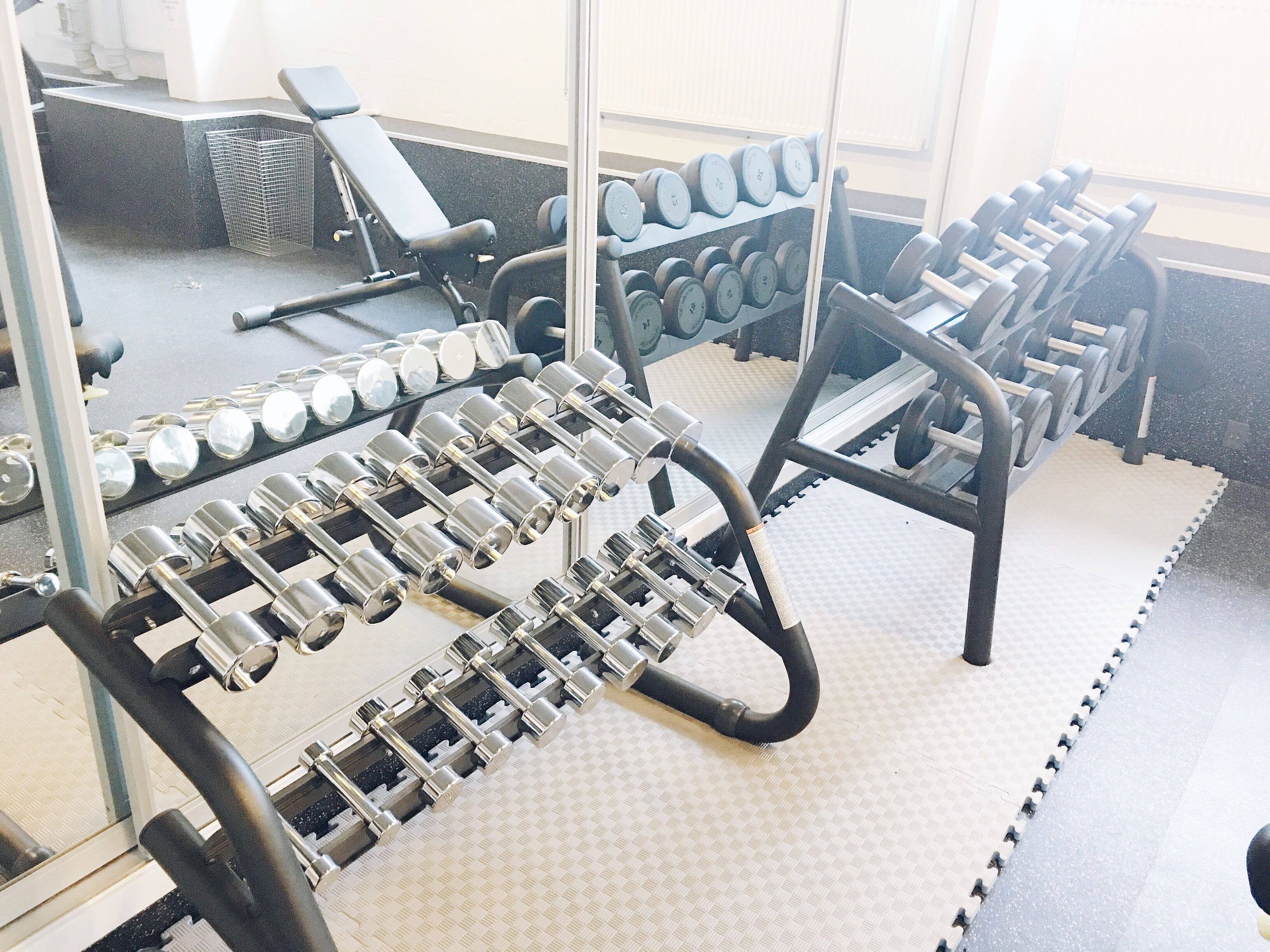 Un gimnasio con varios equipos de levantamiento de pesas, incluyendo mancuernas y un banco.