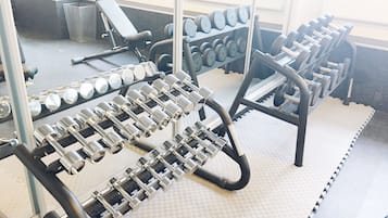 Un gimnasio con varios equipos de levantamiento de pesas, incluyendo mancuernas y un banco.