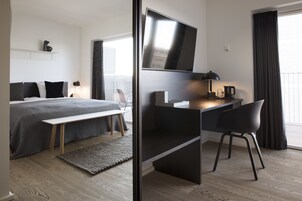 A modern hotel room with a bed, desk, chair, and a TV.