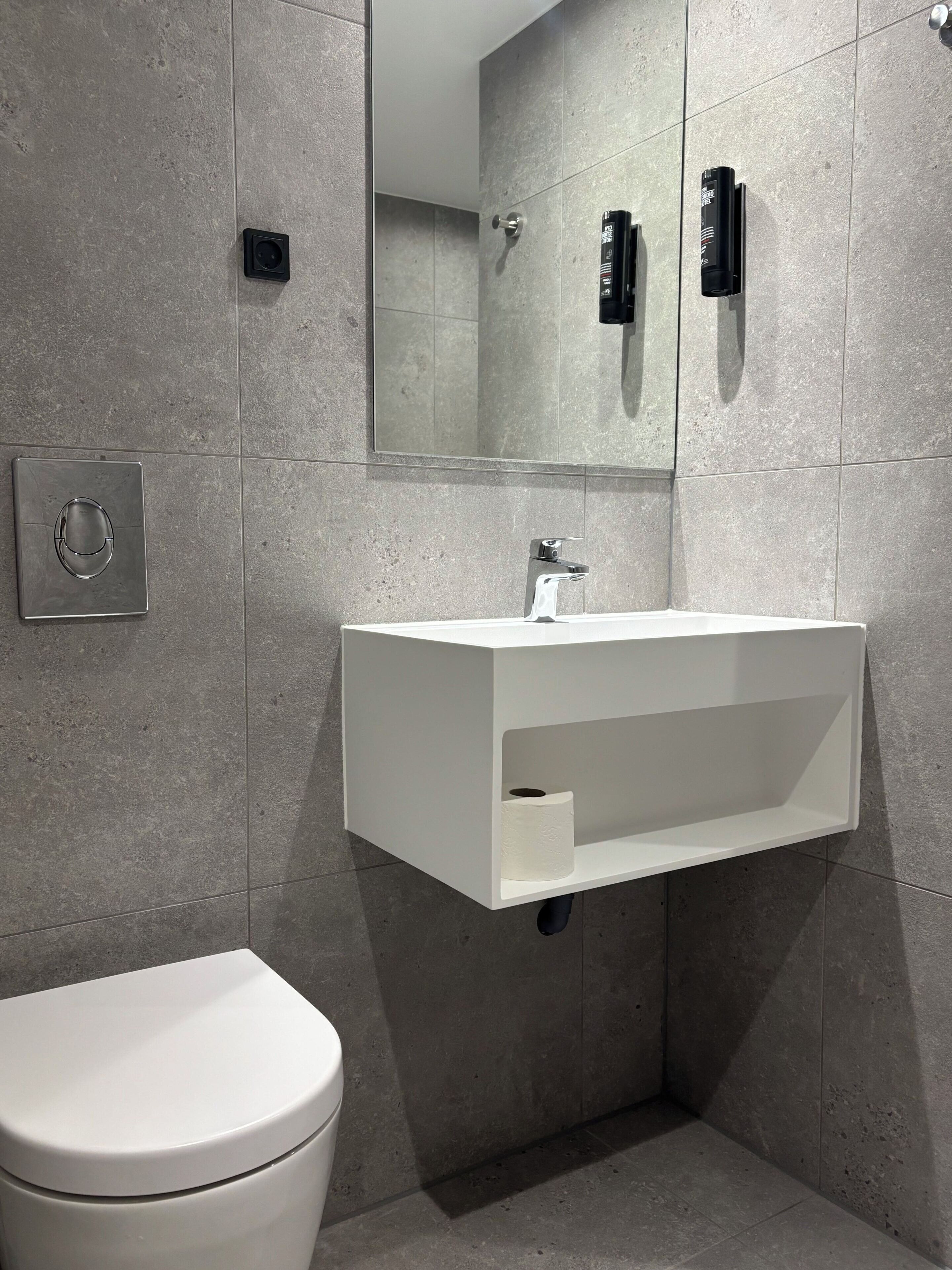 Une salle de bain moderne avec un lavabo blanc, des toilettes et un miroir.