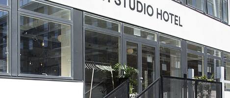 The exterior of the CPH Studio Hotel with large windows, a staircase, and potted plants.