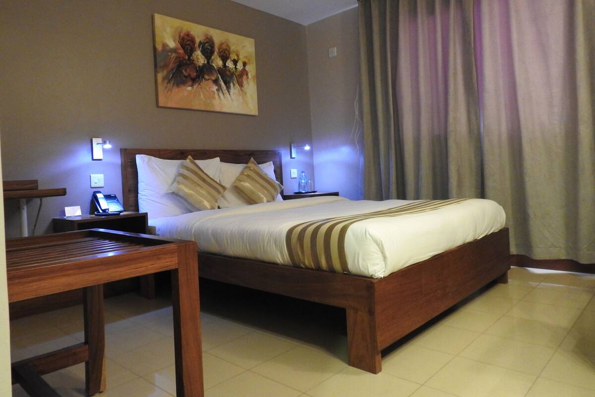 A hotel room with a wooden bed, a bedside table with a phone, and a painting on the wall.