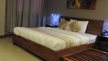 A hotel room with a large bed, wooden headboard, a nightstand with a lamp, and a painting on the wall.
