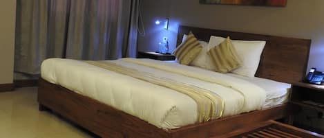 Una habitación de hotel con una cama grande, cabecero de madera, una mesita de noche con una lámpara y un cuadro en la pared.