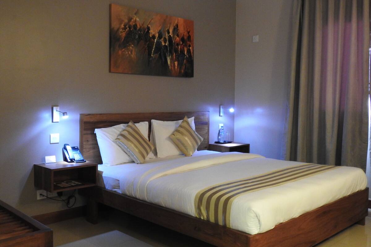 A hotel room with a large bed, bedside lamps, a painting on the wall, and a window with curtains.