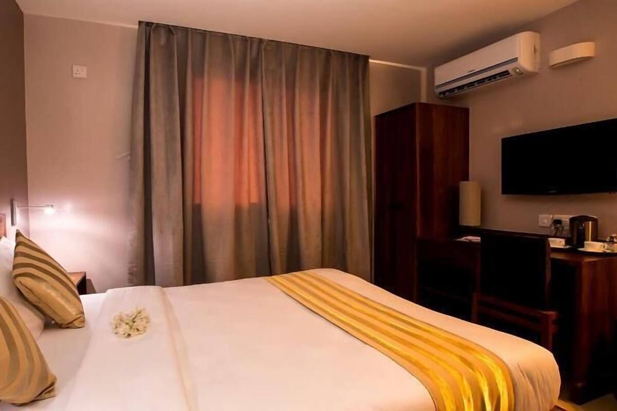 A hotel room with a bed, a desk, a television, and an air conditioning unit.