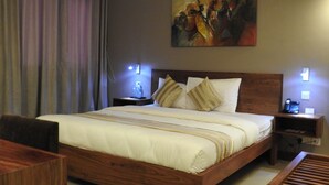 A hotel room with a large bed, wooden headboard, two bedside tables with lamps, a painting on the wall, and a view of the outside through the window. - Venus Premier Hotel (Arusha)
