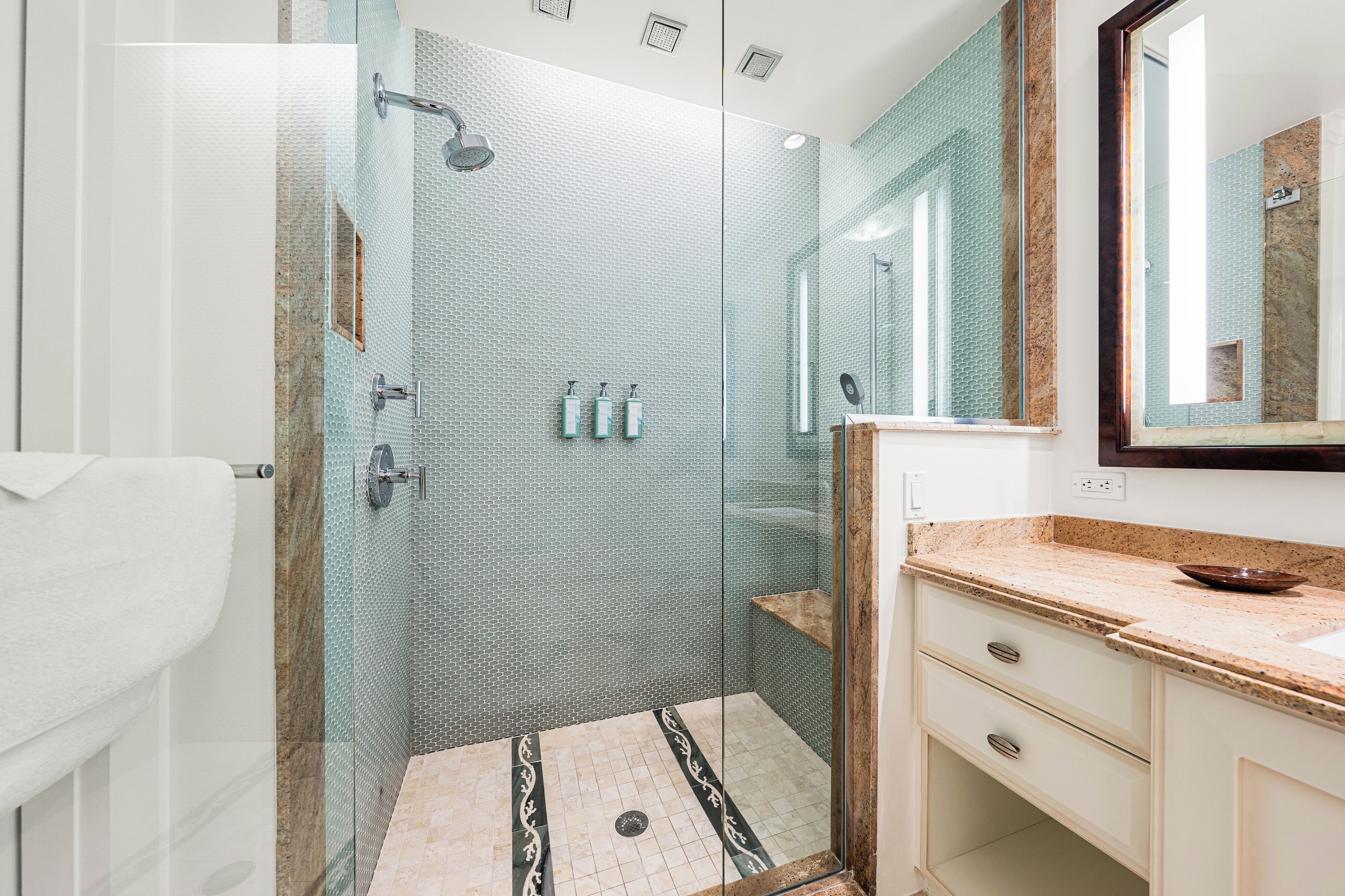 Une salle de bain moderne avec une douche à parois de verre, un comptoir en marbre et un grand miroir.
