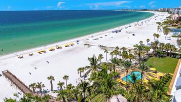 A beach resort with a white sandy beach, palm trees, and a clear blue ocean.