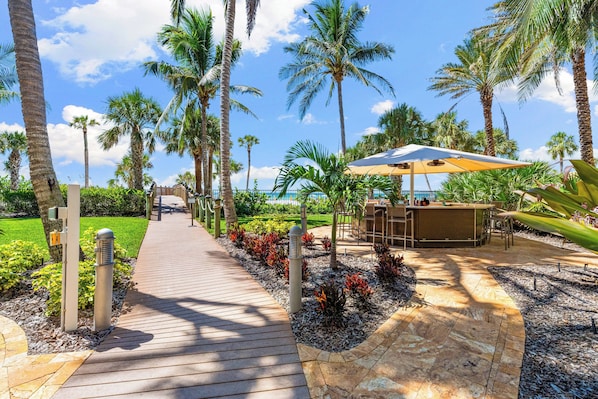 A wooden pathway leading to a bar area with outdoor seating, surrounded by palm trees and a clear sky. - The Residences on Siesta Key within Hyatt Residence Club (Siesta Key)