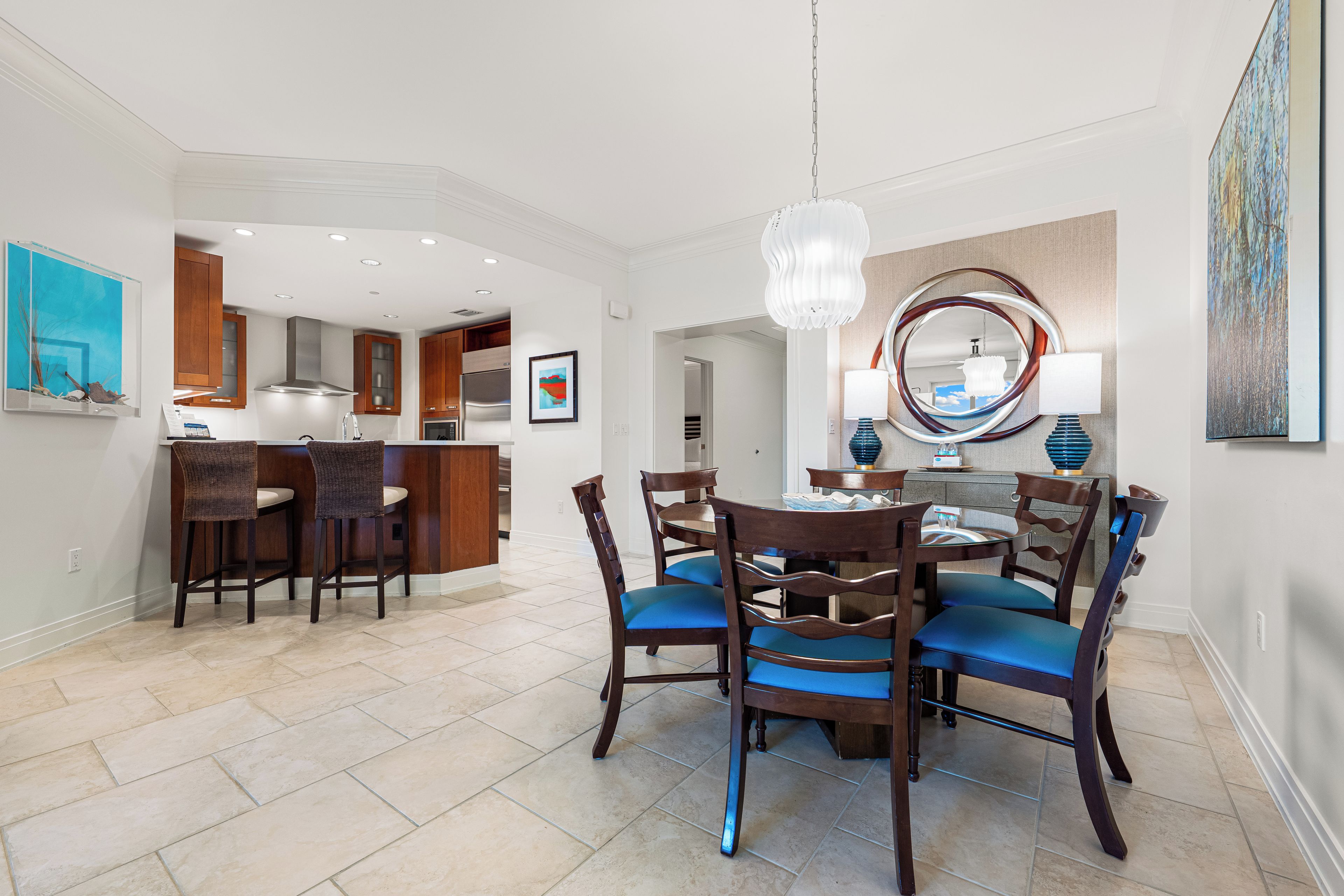 A modern kitchen with a dining area, featuring a round table, wooden chairs, and a chandelier.