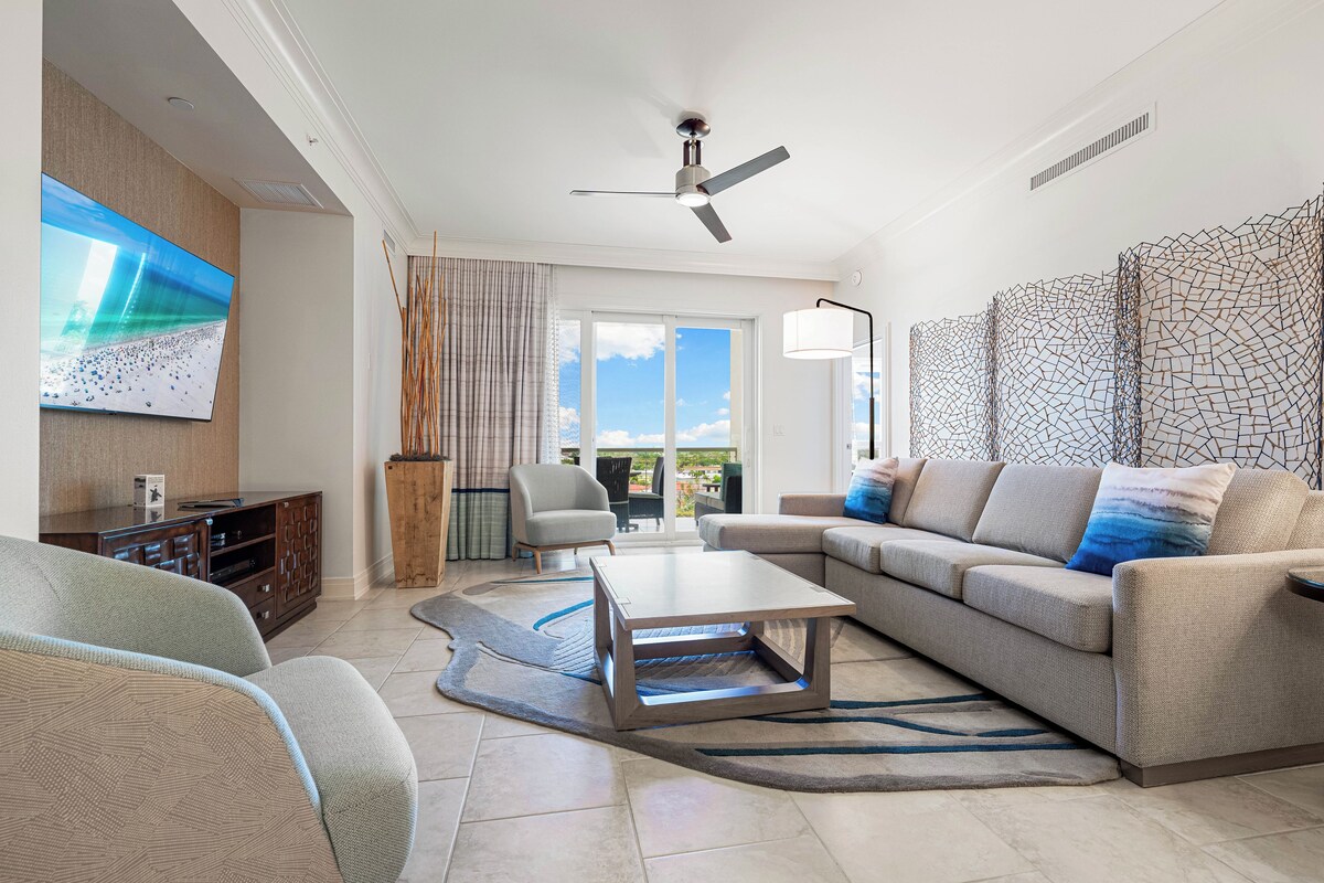 A modern living room with a sectional sofa, a coffee table, a flat-screen TV, and a ceiling fan.