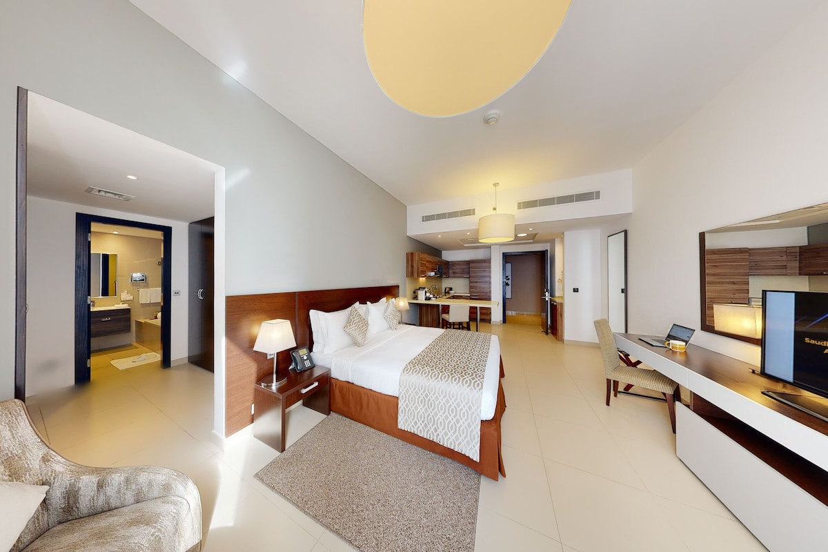 Habitació d'hotel moderna amb un llit gran, un escriptori, un televisor i una zona d'estar separada.