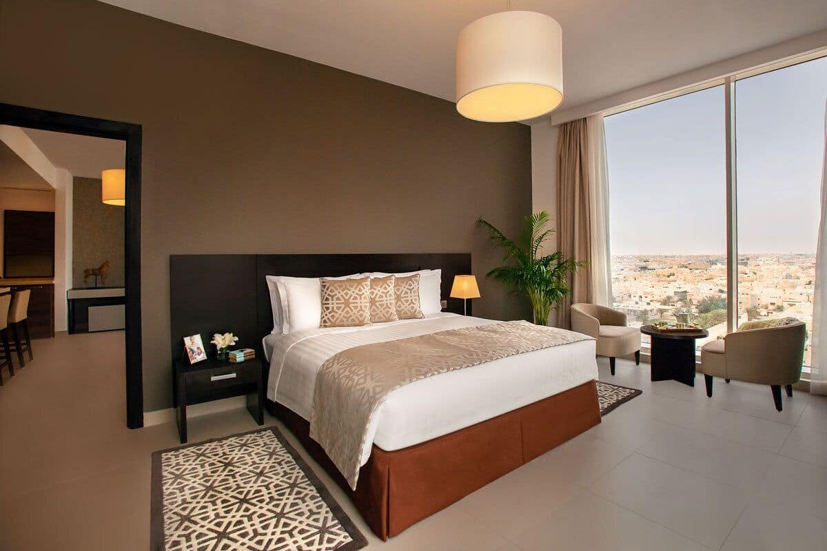 A modern hotel room with a large bed, a desk, a chair, and a view of the city.