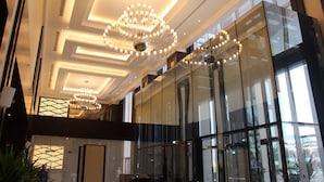 Eine moderne Hotelhalle mit großen Glasfenstern, einem prunkvollen Kronleuchter und einer hohen Decke mit eingelassener Beleuchtung.