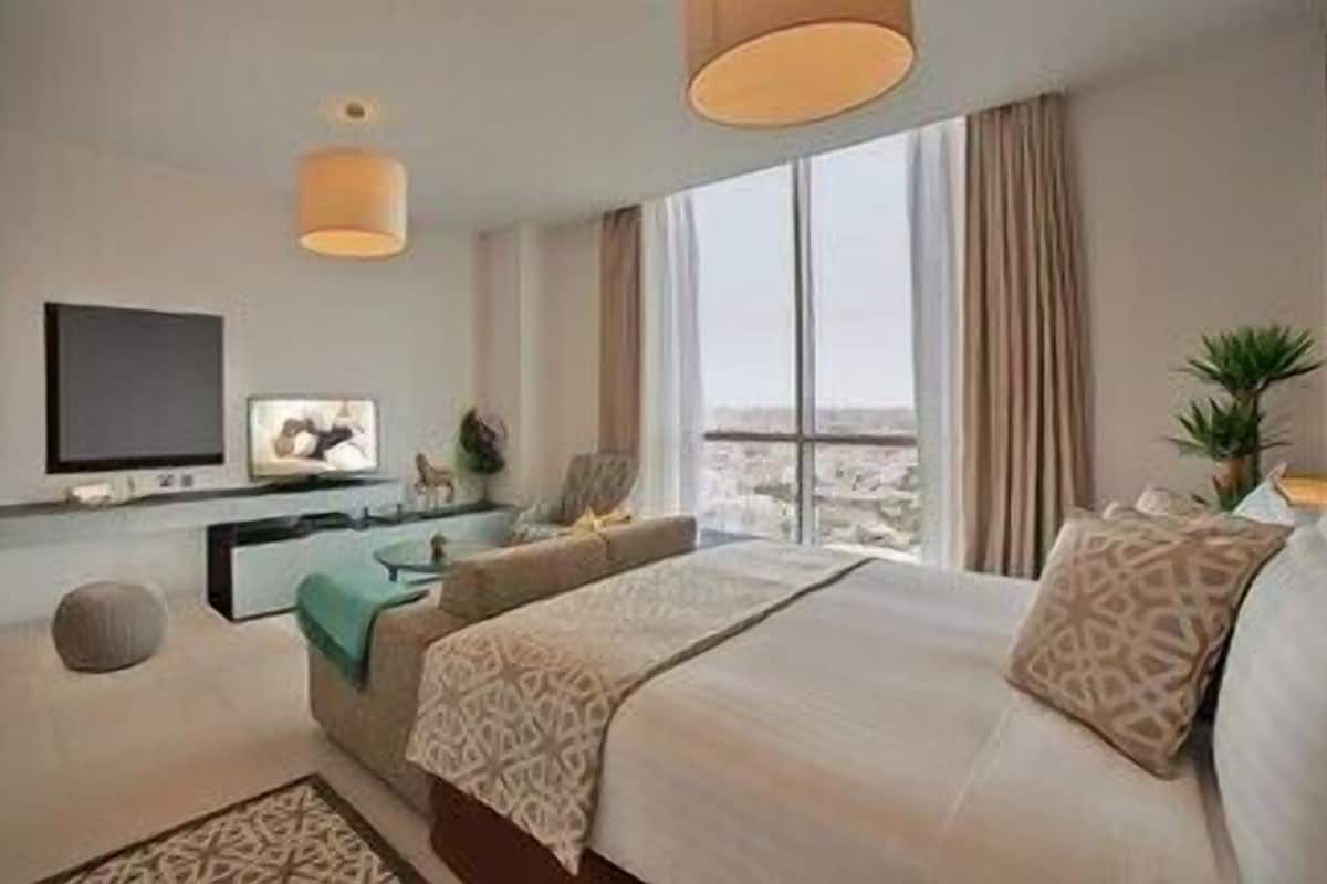 A modern hotel room with a large bed, a television, a desk, and a view of the city.