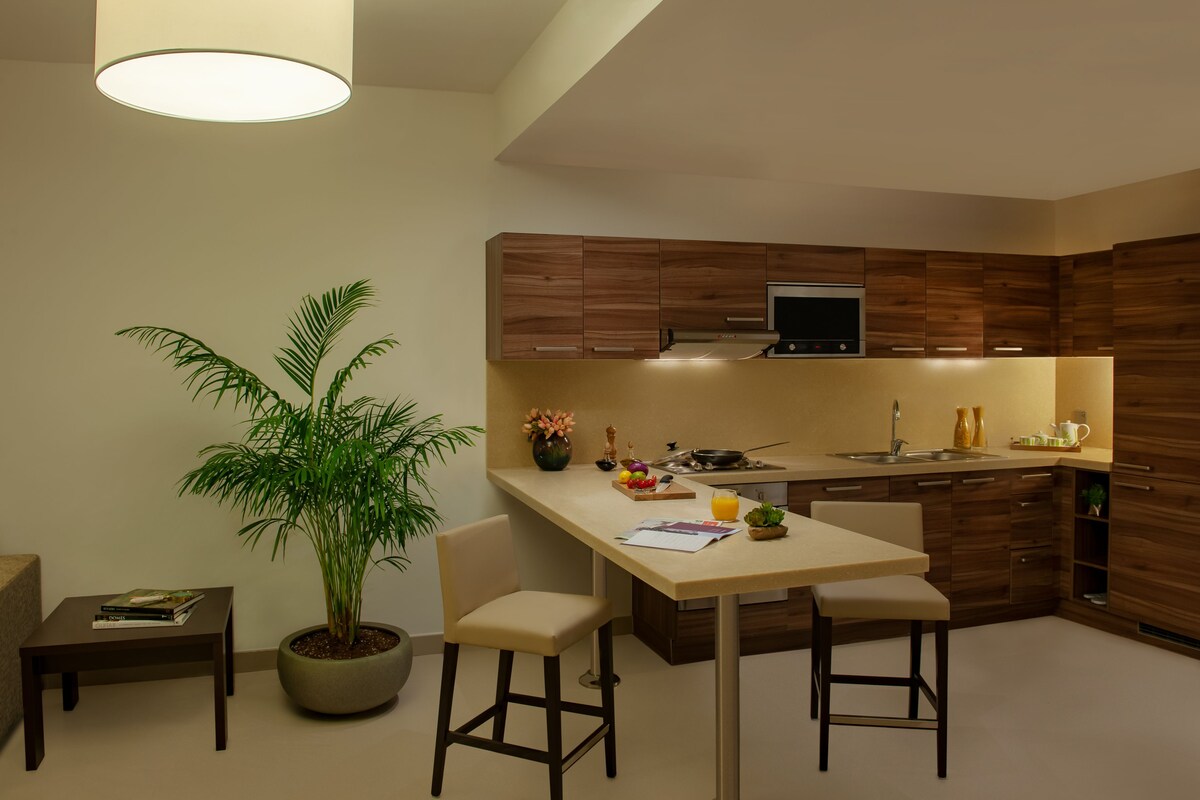 A modern kitchen with wooden cabinets, a built-in oven, and a dining area with a table and chairs.