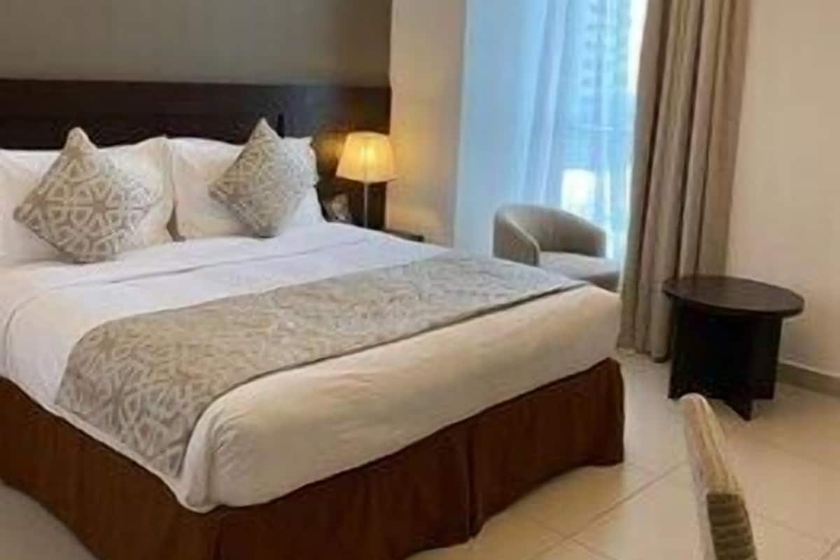 A hotel room with a large bed, a nightstand, a lamp, a chair, and a window with curtains.