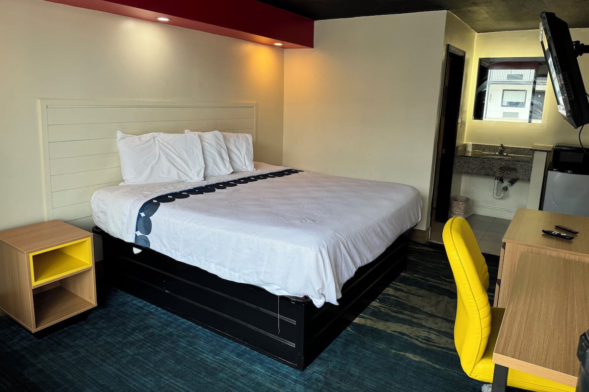 A hotel room with a bed, a desk, a chair, a TV, and a window.