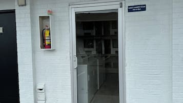 A guest laundry room with an ice machine, a fire extinguisher, and a sign indicating the room's hours of operation.