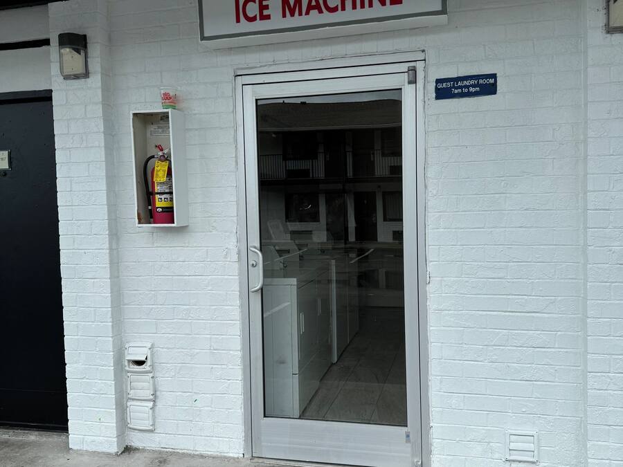 A guest laundry room with an ice machine, a fire extinguisher, and a sign indicating the room's hours of operation.