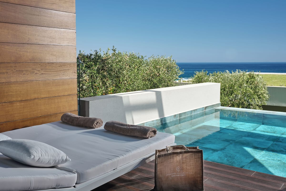 A modern bedroom with a view of the ocean, a pool, and a wooden wall.