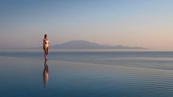 A person walking on a reflective surface by a calm body of water with distant mountains.