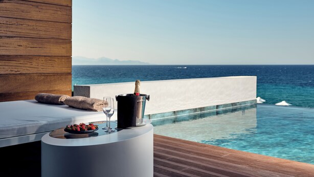 A modern infinity pool with a wooden deck, a lounge area with a cushioned bench, and a bottle of champagne. - Lesante Blu - The Leading Hotels of the World, Adults Only (Zakynthos)