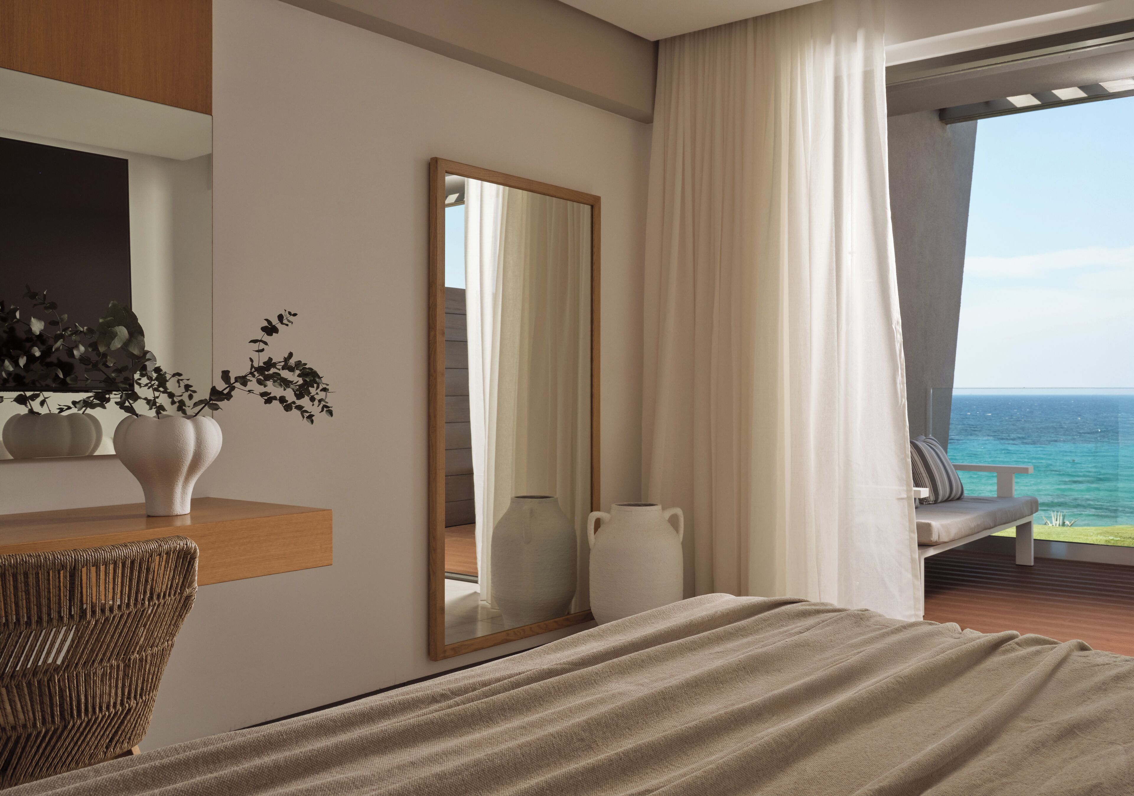Habitación de hotel moderna con una cama grande, un escritorio de madera, un espejo y vistas al océano.