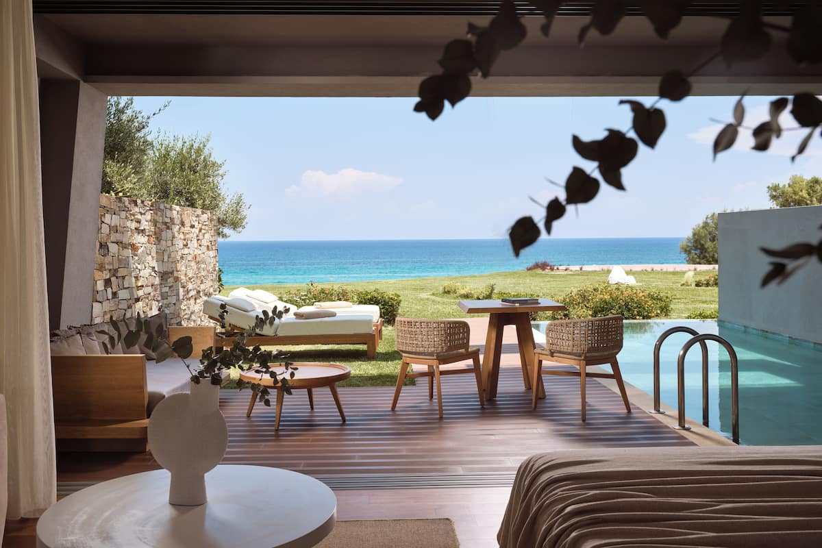 A room with a view of the sea, a pool, and outdoor seating.
