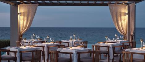 An outdoor dining area with tables and chairs, overlooking the sea.