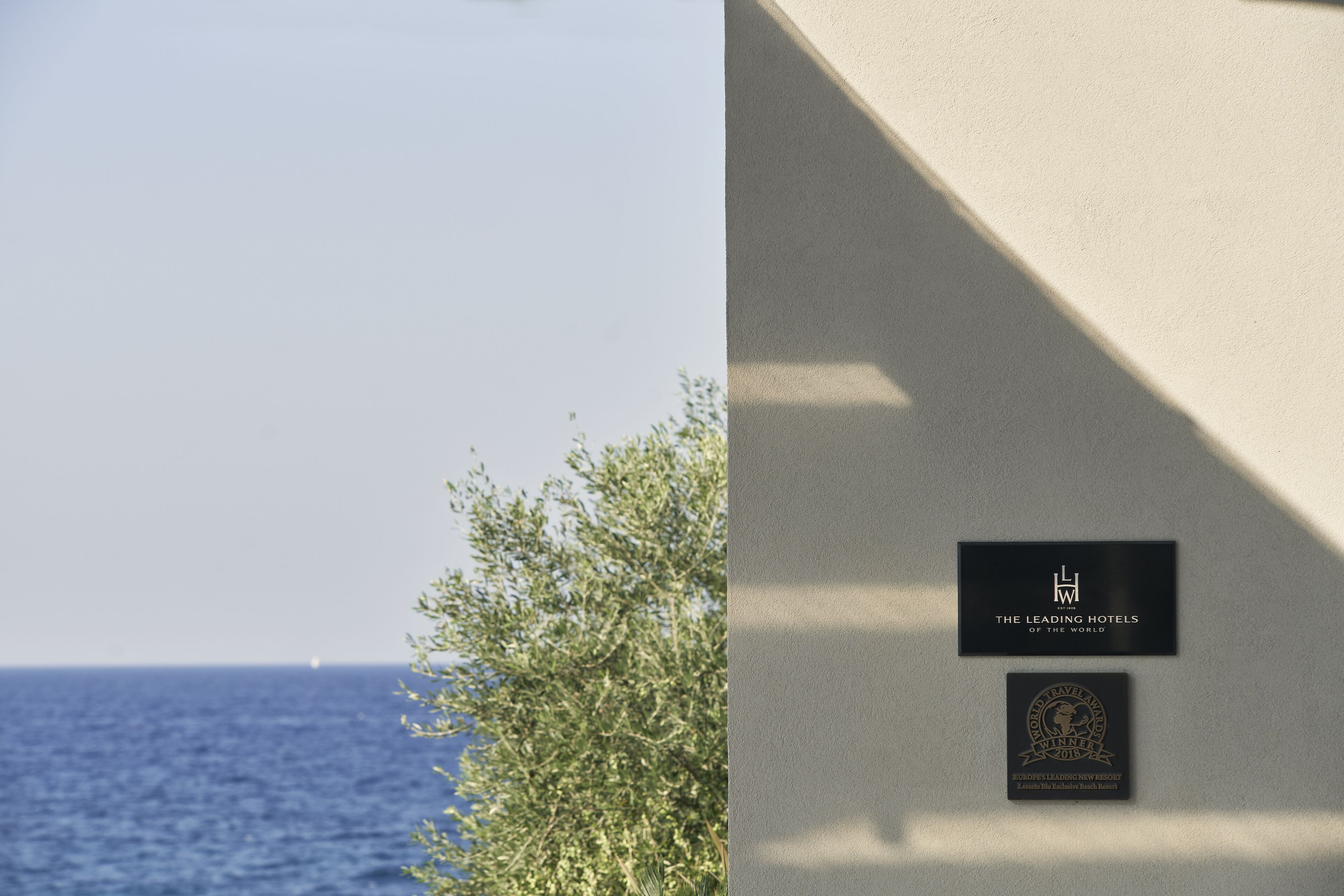 A coastal view with a clear sky, a body of water, and a building with plaques indicating 'The Leading Hotels of the World' and 'Europe's Leading New Resort'.