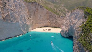 A coastal landscape with a narrow beach flanked by steep cliffs, boats anchored in the turquoise waters, and a clear sky. - Lesante Blu - The Leading Hotels of the World, Adults Only (Zakynthos)